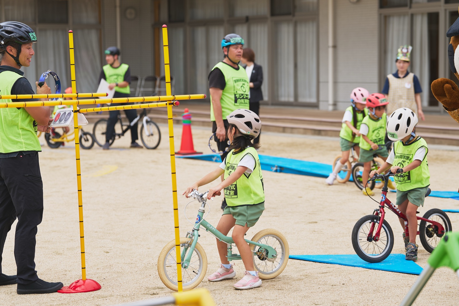 黄色いポールで作った信号機の前で、ペダルなし自転車にまたがった園児が信号の合図を待っている